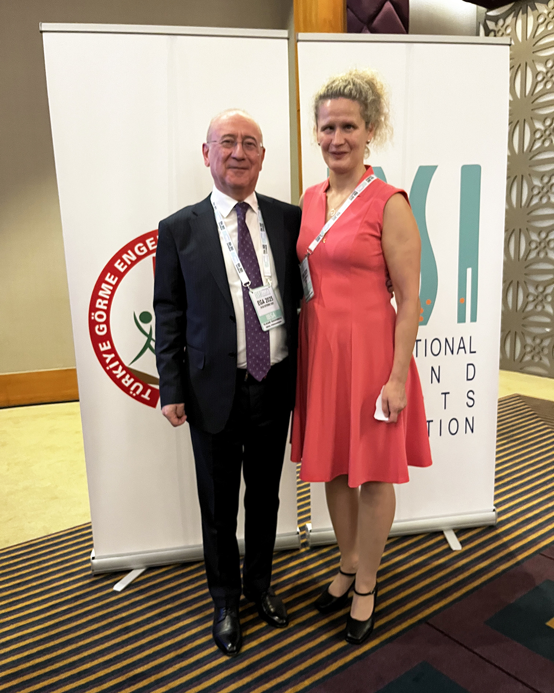 Rahimov ja Tolppanen poseeraavat kokouksen mainosseinäkkeen edessä koristeellisella käytävällä.